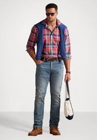 Herreantrekk med en rutete skjorte i røde, blå og grønne nyanser, en blå quiltet vest, lyseblå jeans, brune sko og en lerretstote.