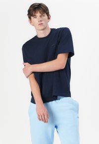 T-shirt en coton bleu marine avec un col rond et des manches courtes, associé à un pantalon de jogging bleu clair avec un petit logo.