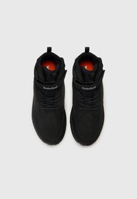 Mustad muste jalatsid pehme ülaosaga, tekstuursed paelad ja rihm. Siseosa on punane ja küljel on silmapaistev Timberlandi logo.