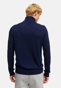 Dunkelblauer Pullover mit einem hohen Kragen und langen Ärmeln, aus einem weichen, strukturierten Stoff. Mit gerippten Bündchen und Saum.