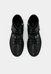 Botas negras hasta el tobillo con un acabado de cuero suave, herrajes plateados y un destacado logotipo de "GUESS" a lo largo de los cordones. Diseño de punta redonda.