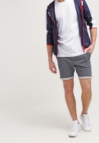 Navy modrá lehká bunda s červenými akcenty, bílý tričko s kulatým výstřihem, šedé texturované šortky a bílé tenisky.