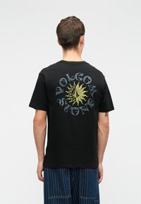 Zwarte katoenen t-shirt met een kleurrijk zonontwerp en de tekst "Volcom Stone" in een cirkelindeling op de achterkant. Korte mouwen, ronde hals.