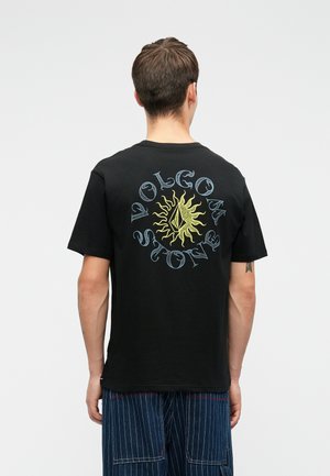 Crna pamučna majica s dugim rukavima koja na leđima sadrži šareni dizajn sunca i tekst "Volcom Stone" u kružnom rasporedu. Kratki rukavi, okrugli ovratnik.