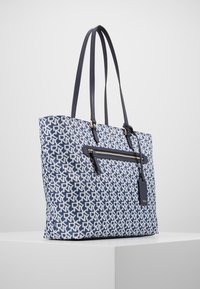 Námořnicky modrá a bílá vzorovaná taška přes rameno s dvojitými uchy, vybavená přední kapsou na zip a zlatými kovovými doplňky. Texturovaný povrch látky.
