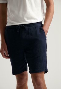 Șorturi texturate de culoare bleumarin, cu talie elastică și șnur de ajustare, dotate cu buzunare laterale și o lungime de până la genunchi. Material ușor.