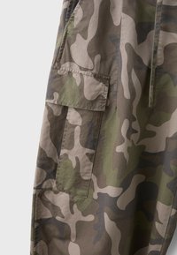 Close-up of pants with green, brown, and beige camouflage pattern and a flap pocket on the side.