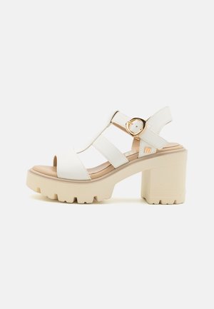 White platform sandals with a chunky heel, featuring a T-strap design, gold buckle accent, and textured sole for grip.
