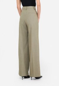Pantaloni larghi color khaki con un design sartoriale, caratterizzati da una texture liscia, una tasca posteriore e un'alta vita. Abbinati a scarpe nere con tacco.