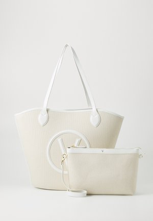 Stor beige tote taske med hvide håndtag og rundt logo, ledsaget af en mindre matchende lynlåspung med håndledsrem.
