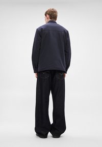 Mornarsko modra lahka jakna z ovratnikom, kombinirana z ohlapnimi temnimi denim kavbojkami z dvema zadnjima žepoma in vidnimi šivi.