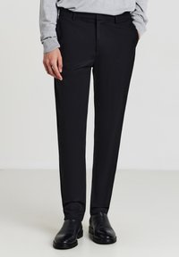 Pantaloni neri su misura con una texture liscia e design a gamba dritta. Presentano passanti per cintura e tasche frontali, indossati con stivali in pelle nera.