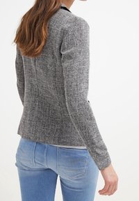 Blazer gris texturé avec une coupe cintrée, fermeture à un seul bouton et manches longues, associé à un jean en denim bleu clair.