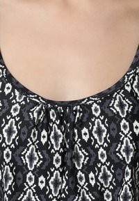 Schwarz-weiß gemusterte Bluse mit einem runden Ausschnitt und gerafftem Detail in der Mitte, aus weichem, glattem Stoff.