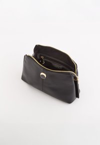 Czarna skórzana torba o gładkiej fakturze, złotym zamkiem błyskawicznym i okrąłym detalem metalowym. Wewnątrz znajduje się kieszeń zapinana na zamek do łatwej organizacji.