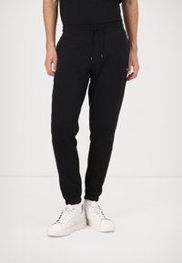 Svarta träningsbyxor med elastisk midja, dragsko och avsmalnande passform. I kombination med vita sneakers med minimalistisk design.