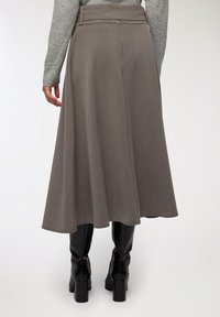 Długa, szara spódnica z teksturowanej tkaniny w kształcie dzwonu. Pas jest płaski, a spódnica swobodnie opada poniżej kolana. Noszona z czarnymi botkami.