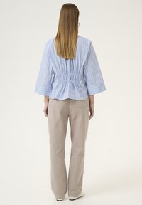 Blusa a righe azzurro chiaro con schiena arricciata, maniche a campana, abbinata a pantaloni beige a gamba larga e sneakers bianche. Tessuto morbido.