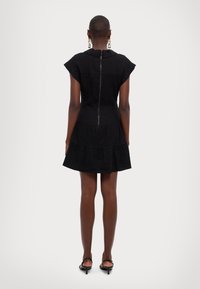 Svart kort klänning med korta ärmar, lager på lager kjol och dragkedja bak. Tillverkad av ett enhetligt tyg med en mjuk yta.