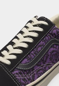 Κοντινή λήψη μαύρου και μωβ αθλητικού παπουτσιού με λευκές κορδόνια, μαύρη δερμάτινη ρίγα και μωβ ύφασμα με μαύρα αφηρημένα σχέδια.