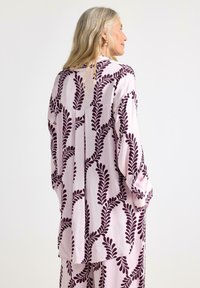 Lyserød bluse med et mørkeburgunder bladmønster. Løs pasform, lange ærmer og en let afrundet kant skaber en afslappet silhuet.