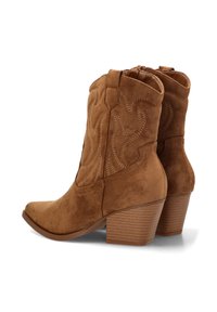 Botas de ante marrón hasta el tobillo con punta afilada, costuras decorativas y un tacón apilado. Cierre con cremallera lateral. Parte superior y tacón texturizados.