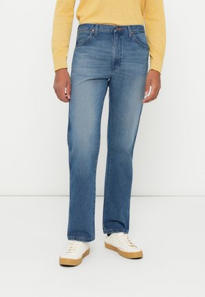 Blaue Jeans aus Denim mit gerader Beinform, mittlerer Waschung, Five-Pocket-Stil und dezenten Nähten. Getragen mit cremefarbenen Sneakers.