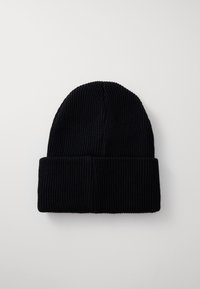 Svart ribbet strikket lue med brett. Laget av mykt materiale, den har vertikale linjer og et tettsittende design.