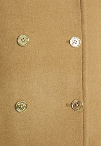 Manteau en laine beige avec quatre boutons dorés brillants disposés en style croisé.