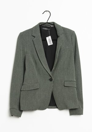 Blazer pour femme texturé gris et blanc à un seul bouton, avec revers crantés, poches à rabat sur le devant, suspendu à un cintre noir avec étiquette de prix.