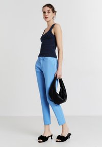 Top in tessuto navy, pantaloni su misura azzurri chiari, borsa nera, sandali neri con tacco e dettagli floreali, texture minima, silhouette moderna.