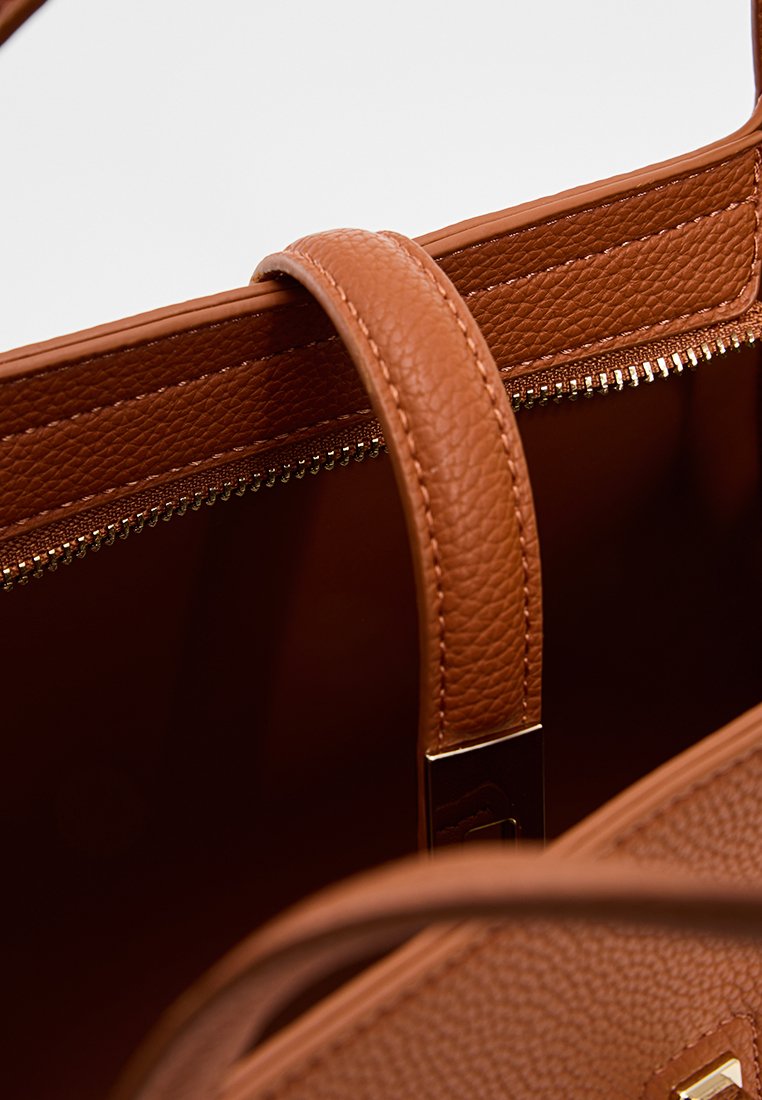 Intérieur d'un sac à main en cuir marron avec un compartiment zippé, présentant une texture lisse, une forme structurée et une seule anse supérieure.