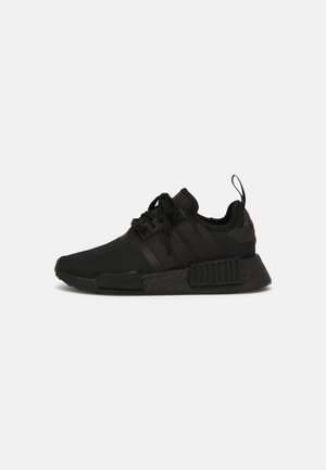 Baskets de sport noires avec semelle texturée, lacets à l’avant, languette au talon et design à trois bandes sur le côté, vues de profil.