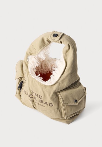 Sac d'épaule en toile beige avec doublure intérieure blanche duveteuse, poche avant, fermeture éclair et détail à bouton, étiqueté "The Pack Bag Marc Jacobs."