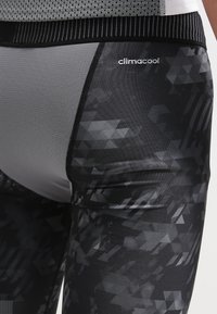 Czarne legginsy graficzne z teksturowanym geometrycznym wzorem, z gładkim wykończeniem i oddychającym pasem z siateczki. Widoczne logo.