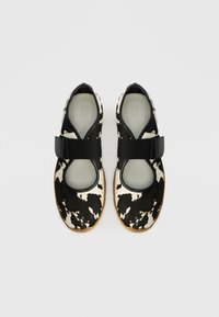 Sapatos com padrão de vaca preto e branco, com parte superior suave, bico redondo e correia ajustável preta. Palmilha de cor clara e sola de borracha.