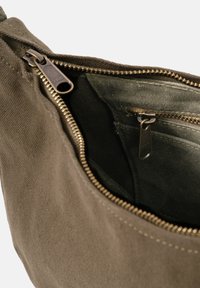 Canvas bag interior in olive green featuring a metal zipper with gold-toned teeth and a small inner pocket with a matching zipper.