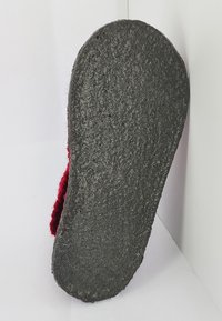 Zwarte rubberen zool met een gestructureerd oppervlak en ronde randen, met een klein rood stoffen accent aan de zijkant.