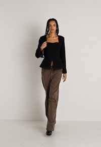 Melnā pepluma žakete ar kvadrātveida dekoltē un pogu aizdari, kombinēta ar brūniem biksēm; gluda struktūra, pieguļošs griezums un elegants dizains.