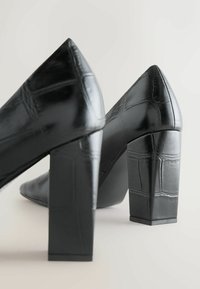 Czarne buty na wysokim obcasie z zaostrzonym noskiem, wykonane z teksturowanej sztucznej skóry krokodyla, z masywnym słupkowym obcasem i błyszczącym wykończeniem.