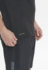 Svart snabbtorkande träningsskjorta med en slät yta, med sid söm och tryckt etikett. Shorts i matchande färg, med enhetlig stil.