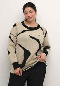 Pull en tricot beige avec des motifs abstraits noirs, col et poignets à côtes noires contrastants ; coupe décontractée avec une texture douce.
