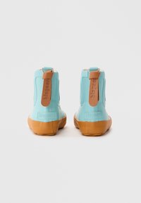 Bottes de cheville en caoutchouc bleu avec des semelles texturées marron et une languette en cuir tan, arborant un branding audacieux à l'arrière. Fini lisse, design pratique.