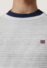 Biały sweter dzianinowy z teksturowanym wzorem w paski oraz granatowym kołnierzykiem. Na piersi wyszyty jest mały emblemat norweskiej flagi.