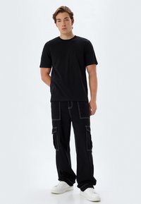 Sort bomulds T-shirt parret med sorte cargo bukser, der har hvid syning og flere lommer, fuldendt med hvide sneakers.