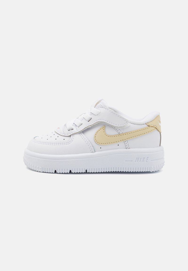 White leather sneaker with a smooth texture, featuring a yellow accent Nike swoosh, round toe, flat laces, and a textured white rubber sole.
