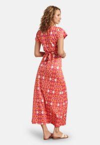 Maxi-Kleid in lebhaftem Pink mit geometrischem Muster. Kurze Ärmel, tailliert mit Gürtel und aus glattem Stoff. Getragen mit leichten Sandalen.