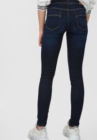 Vaqueros skinny azul oscuro de cintura alta, con dos bolsillos traseros y detalles de costura mínimos, combinados con zapatillas deportivas blancas.