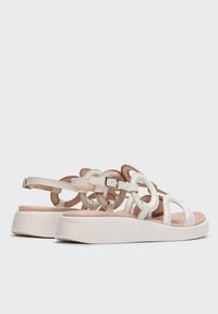 Sandalias de cuero blanco con recortes circulares y acentos en tono marrón. Cuenta con una correa ajustable y una suela gruesa blanca con una superficie texturizada.