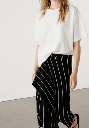 White, short-sleeve t-shirt paired with black striped wide-leg pants featuring a diagonal overlay. Textured fabric and simple design.